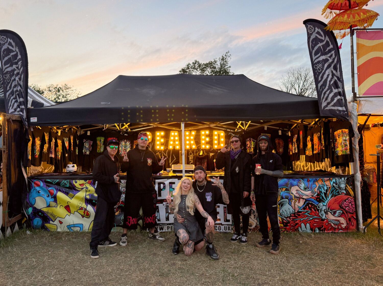 The Peaked crew at the festival stall, under the lit-up PEAKED sign